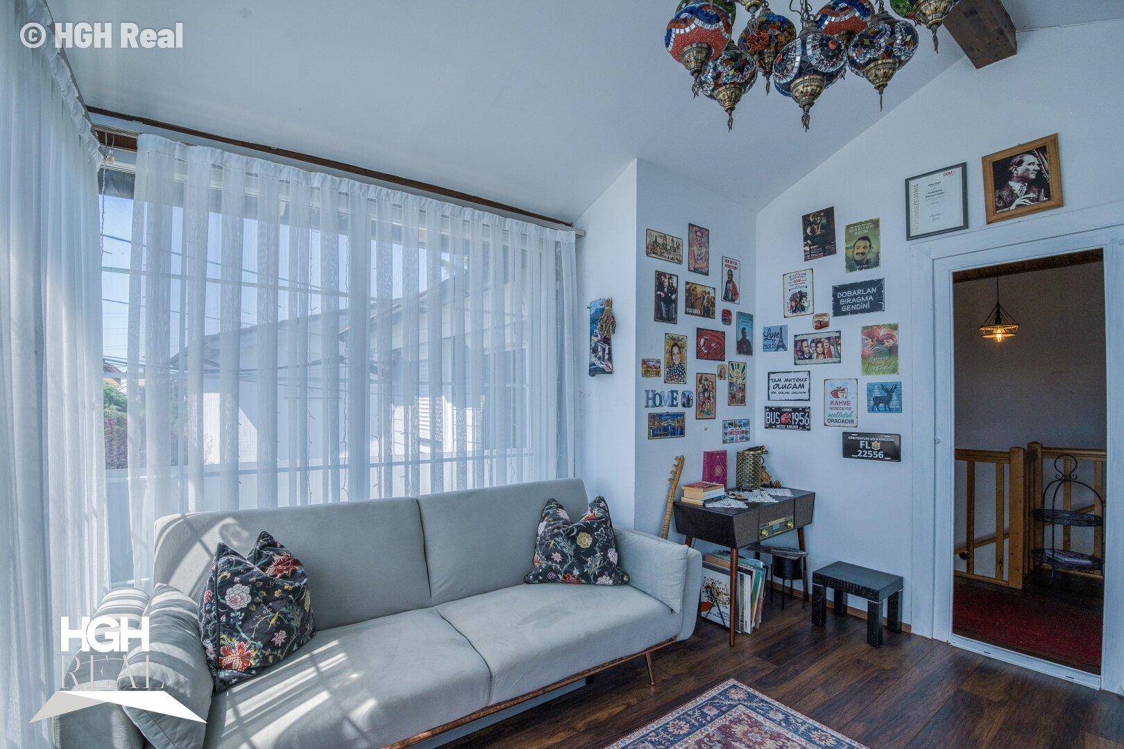 Gemütlicher Wintergarten mit Sofa, Teppich und einer kreativ gestalteten Bilderwand.