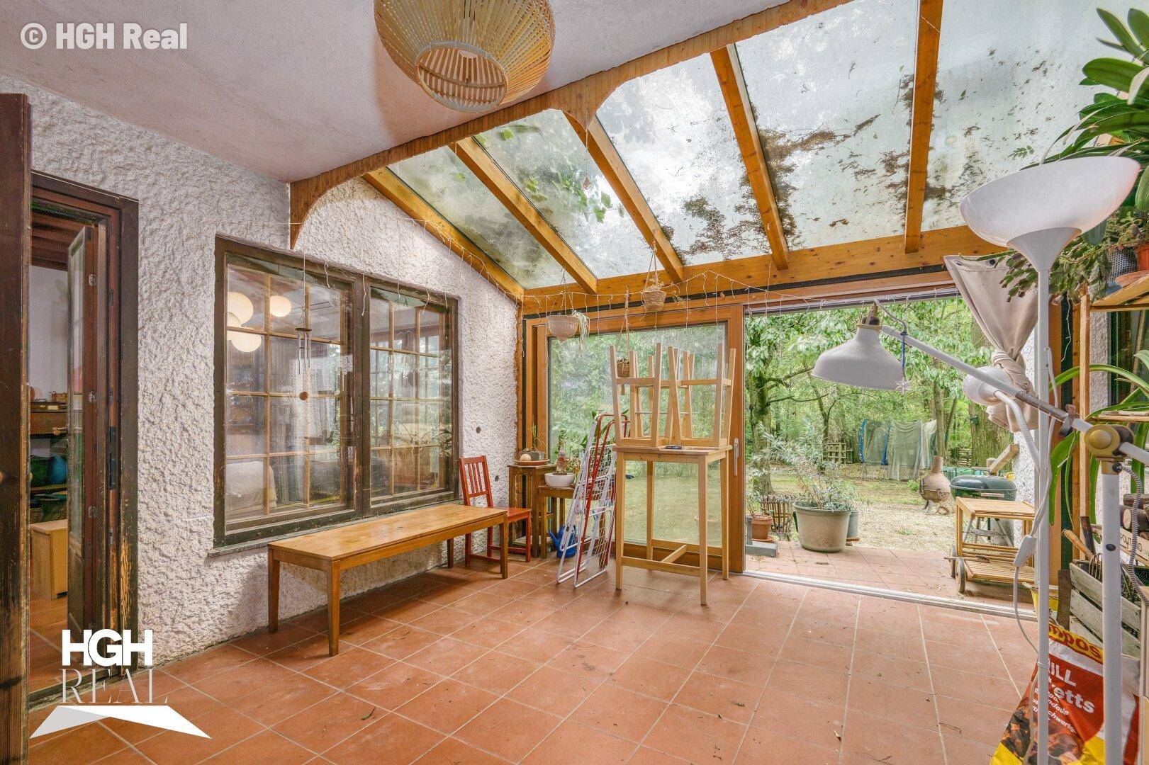 Heller Wintergarten mit Glasdach, Fliesenboden und Zugang zum Gartenbereich.