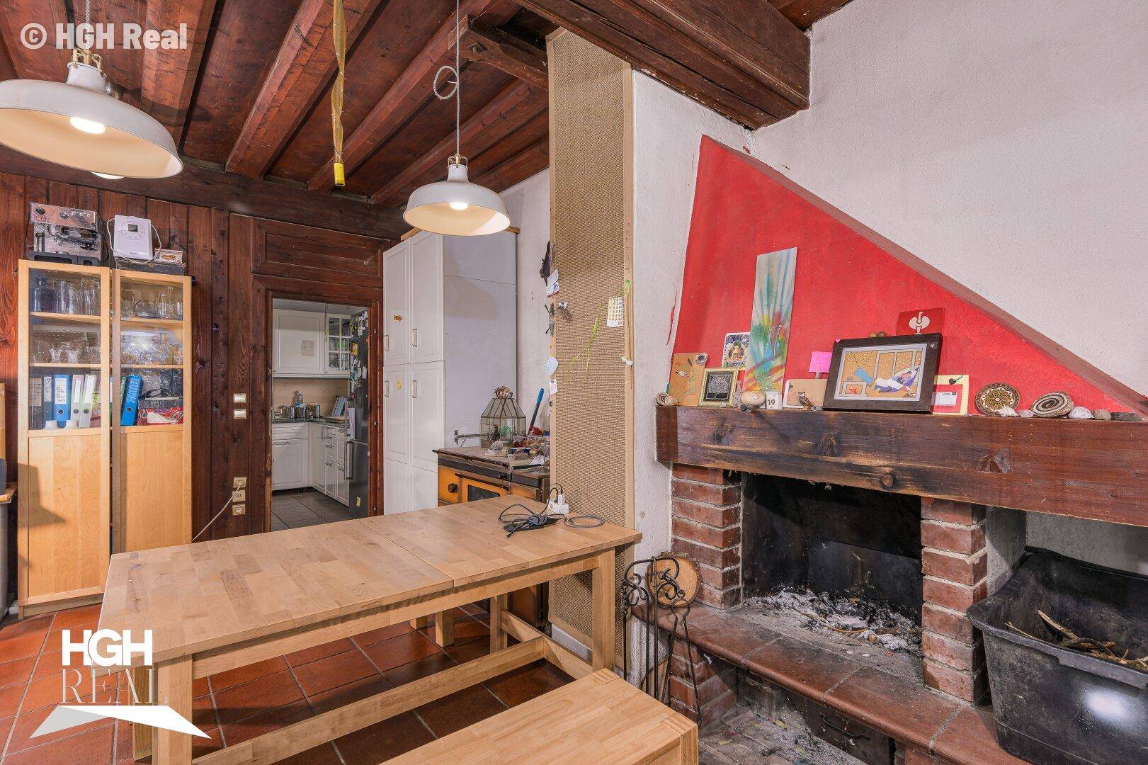 Wohn- und Essbereich mit rustikalem Kamin, Holzbalkendecke und Fliesenboden.
