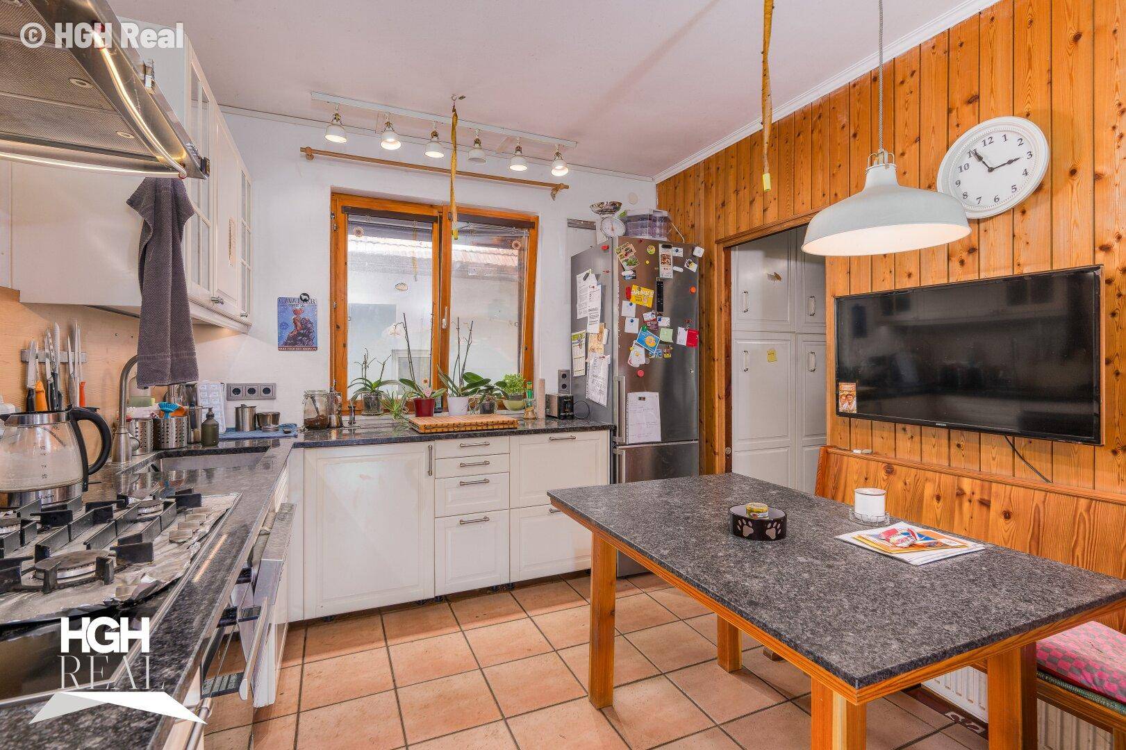 Küche mit weißen Schränken, dunkler Arbeitsplatte und Holzvertäfelung.