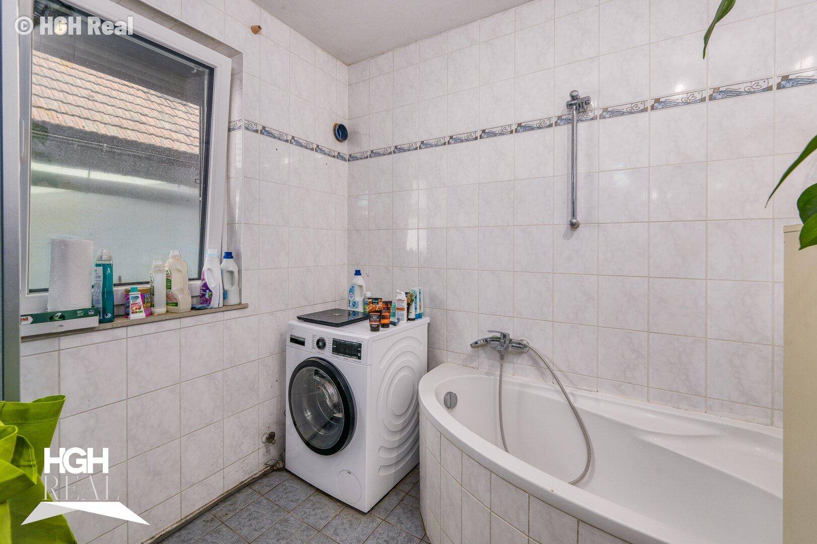 Badezimmer mit Badewanne, Waschmaschine und Fenster.