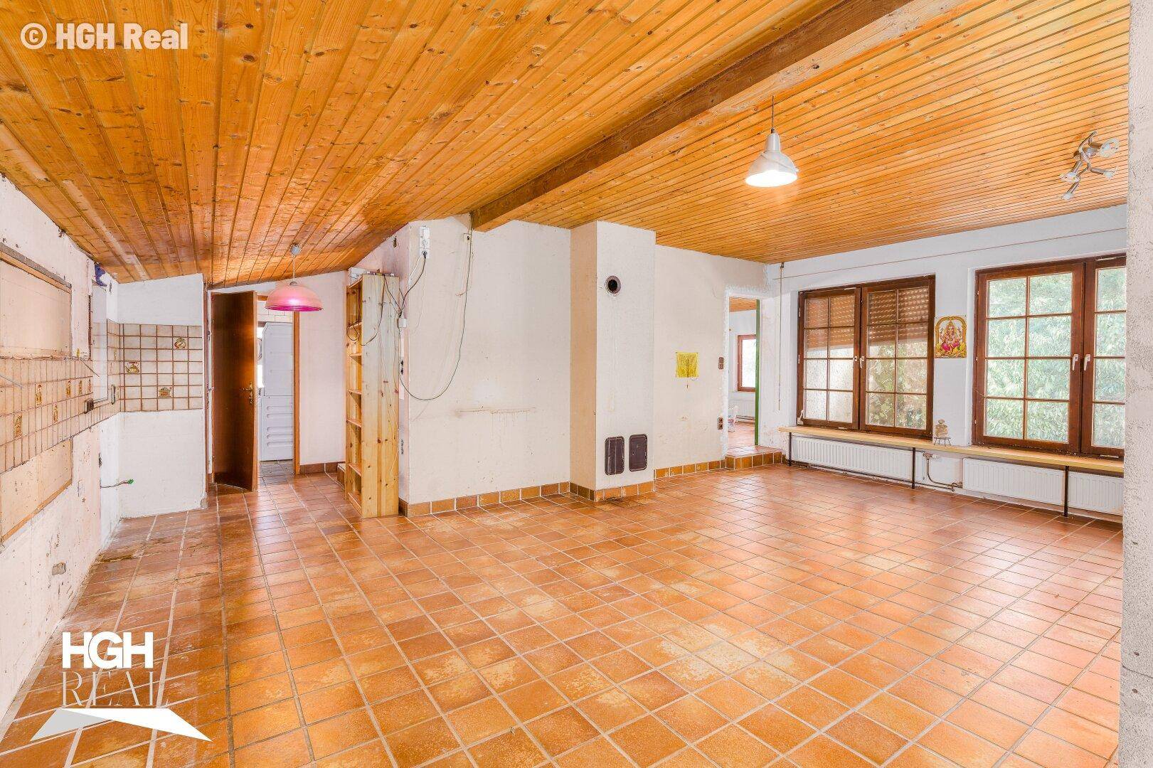 Geräumiger Wohnbereich mit Fliesenboden, Holzdecke und vorbereiteten Wänden.