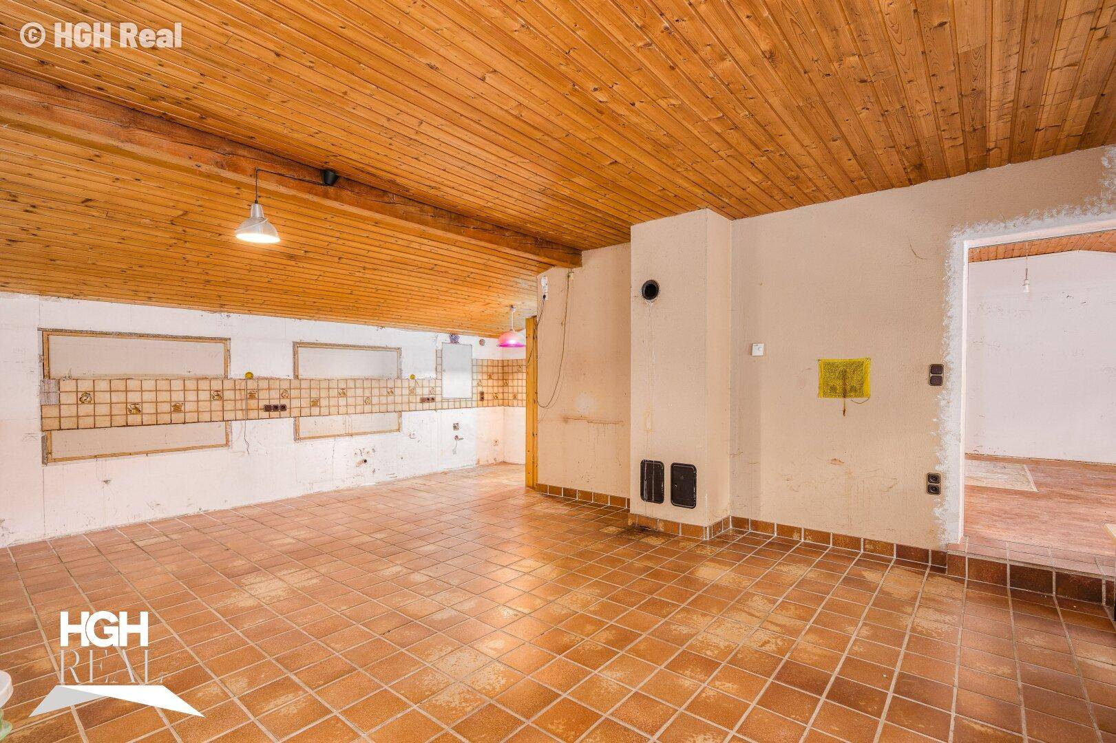 Großer offener Raum mit Fliesenboden, Holzdecke und vorbereiteten Wänden für Renovierung.