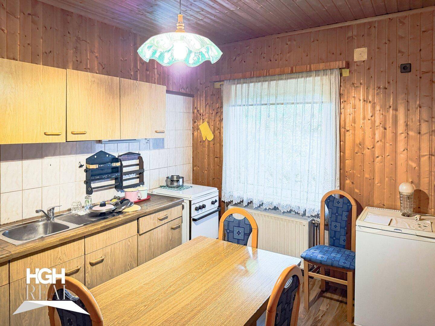 Rustikale Küche mit Holzvertäfelung, Esstisch und einfachen Küchengeräten, bietet gemütliche Atmosphäre.