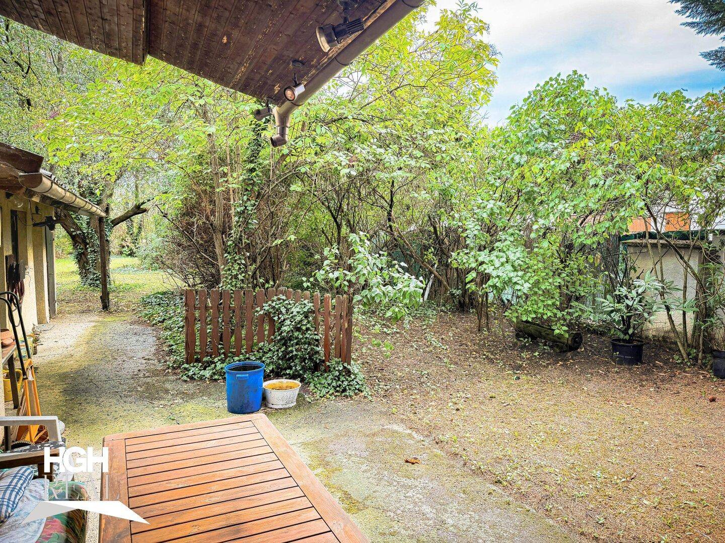 Blick von einer überdachten Terrasse in den weitläufigen Garten mit üppiger Vegetation und Bäumen.