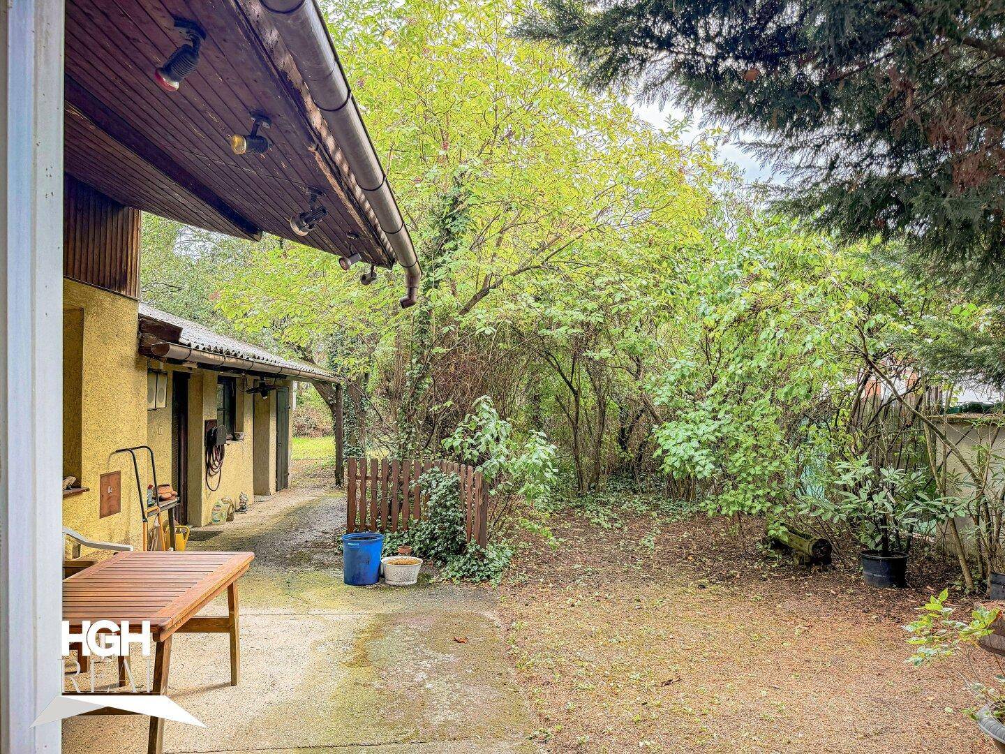 Weitläufiger Gartenbereich mit üppigem Grün und einem überdachten Sitzbereich am Haus.
