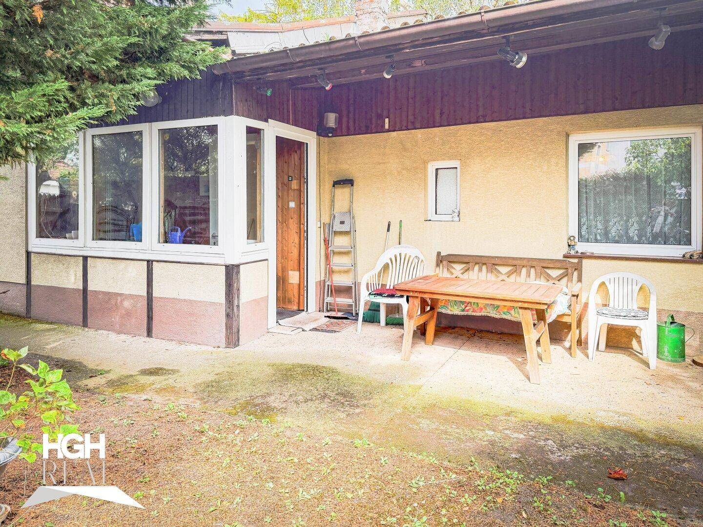 Überdachte Terrasse mit Gartenmöbeln und Zugang zum Haus, umgeben von Grünflächen.