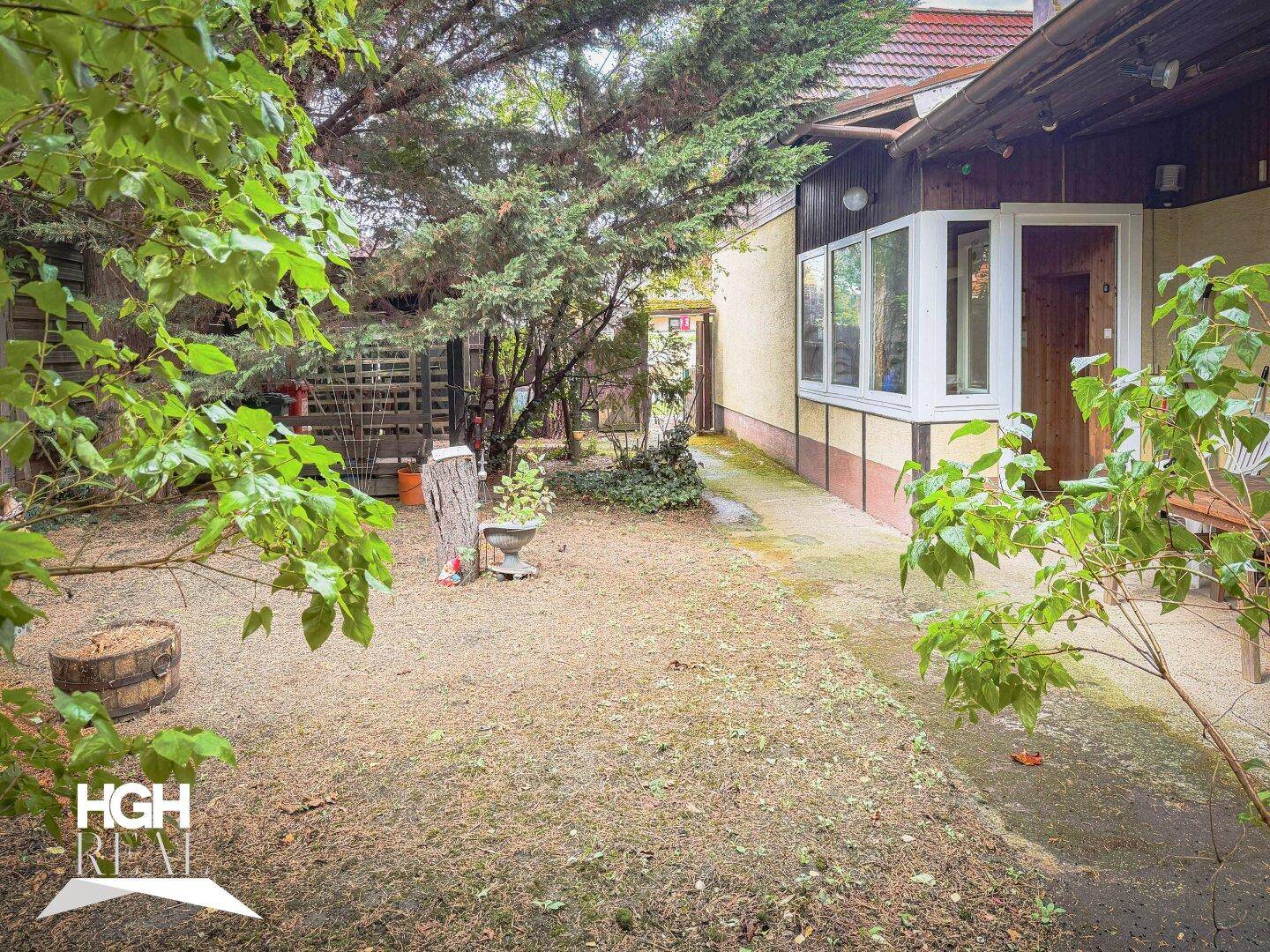 Seitlicher Gartenbereich mit kleiner Terrasse und Zugang zum Haus, umgeben von Bäumen und Sträuchern.