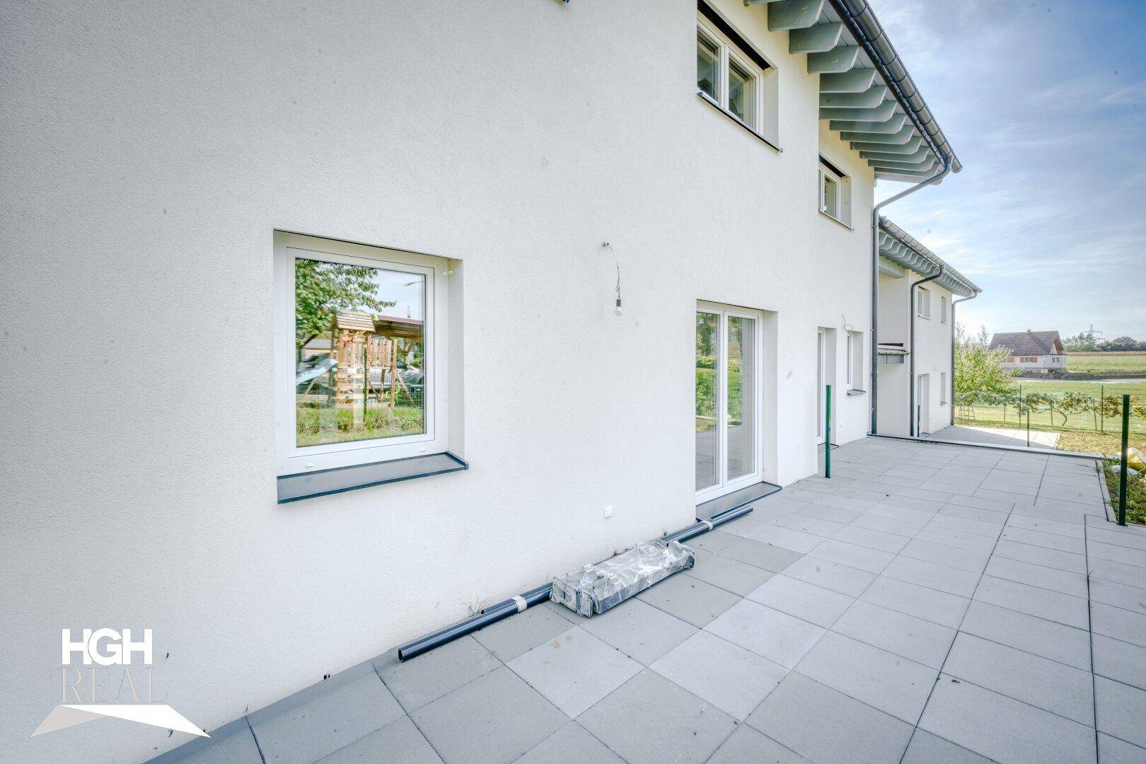 Helle Terrasse mit weißer Fassade und Blick ins Grüne, ideal für entspannte Stunden im Freien.