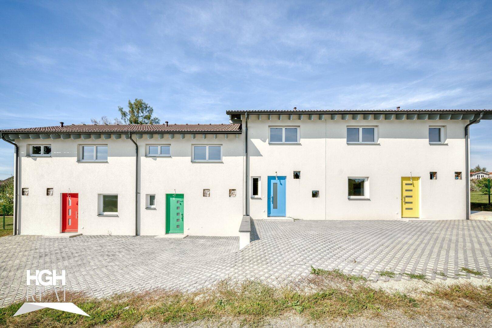Moderne Reihenhäuser mit weißer Fassade und farbigen Eingangstüren unter blauem Himmel.