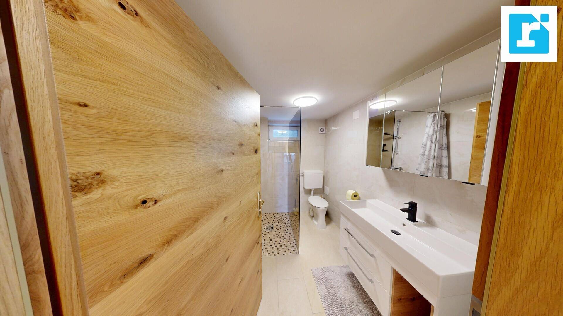 Modernes Badezimmer mit Holzwand, weißem Waschtisch, Spiegelschrank und begehbarer Dusche.