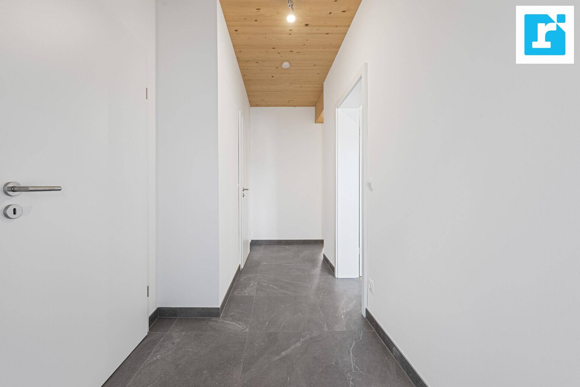 Heller Flur mit Holzbalkendecke und modernem Fliesenboden.