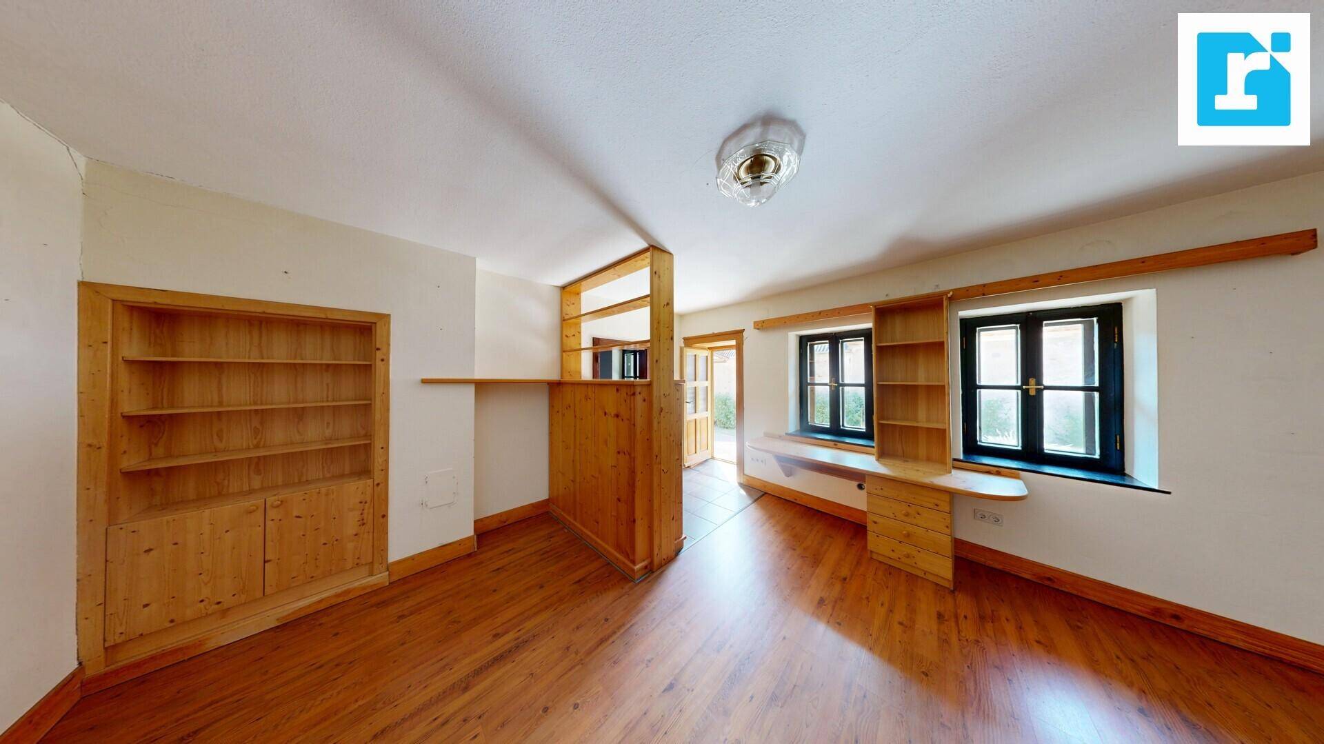Helles Zimmer mit Holzeinbauregalen, Holztrennwand und Fenstern für natürliches Licht.