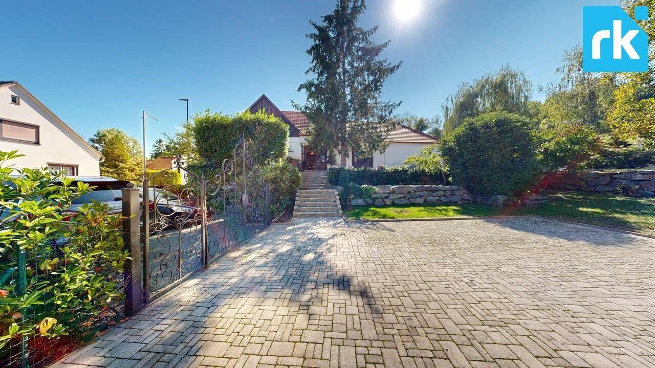 Zufahrt zum Anwesen mit schmiedeeisernem Tor, gepflasterter Auffahrt und Treppe zum Haupthaus.