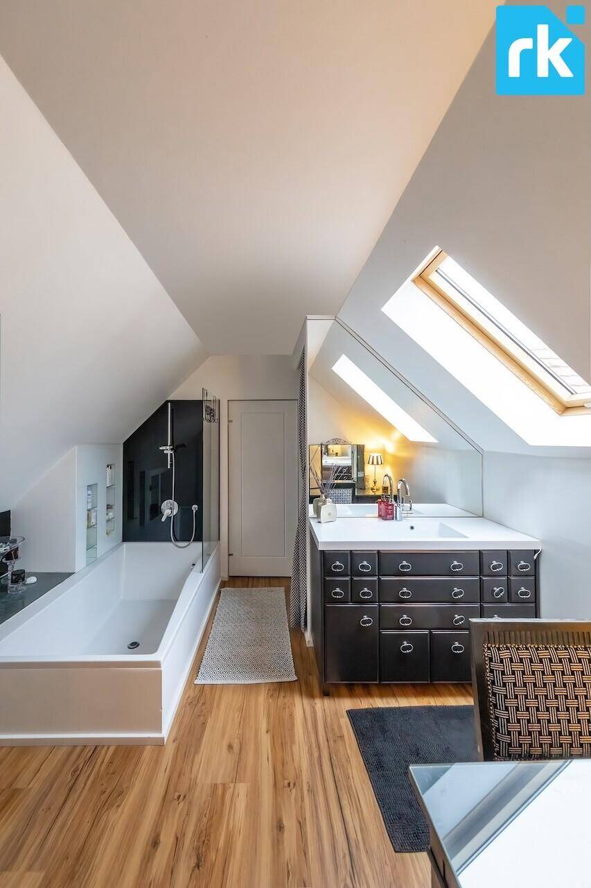 Modernes Badezimmer im Dachgeschoss mit Badewanne, Waschtisch und viel Tageslicht durch Dachfenster.