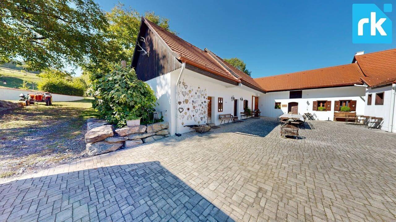 Außenansicht des Anwesens mit gepflastertem Bereich, dekorierter Fassade und umgebender Natur.