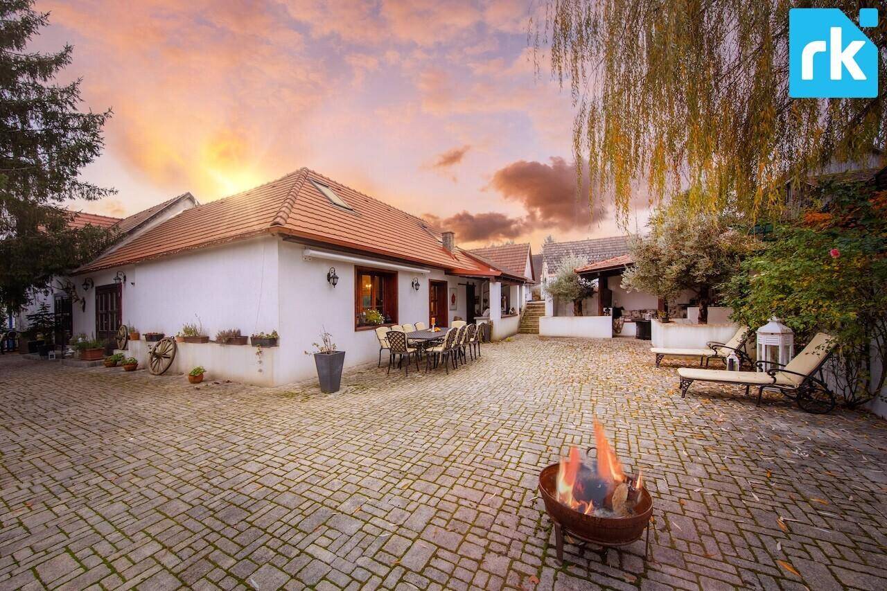 Malerisches Anwesen bei Sonnenuntergang mit Feuerstelle im gepflasterten Innenhof und altem Baumbestand.