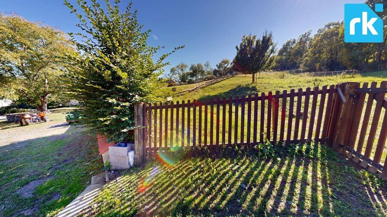 Ländliche Szene mit Holzzaun, grünen Wiesen und Bäumen unter strahlendem Sonnenschein.