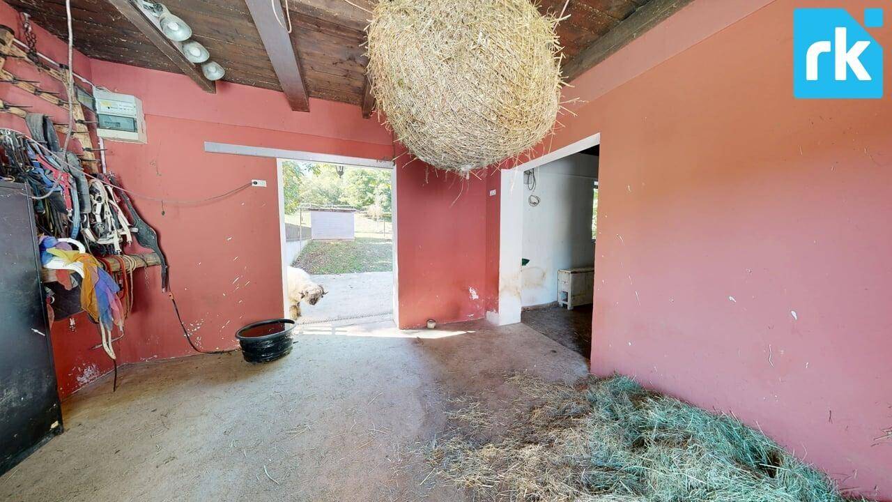 Innenansicht eines Stalls oder einer Scheune mit Heu auf dem Boden und roten Wänden.