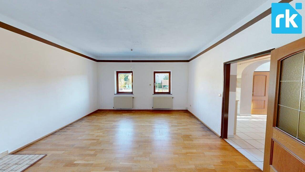 Helles Wohnzimmer mit Holzboden und zwei Fenstern, die viel Tageslicht hereinlassen.