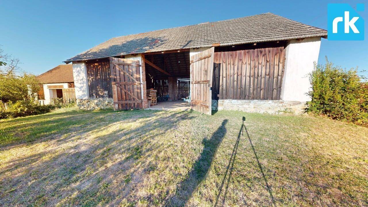 Rustikale Scheune mit großen Holztoren und weitem Grasland im Vordergrund.