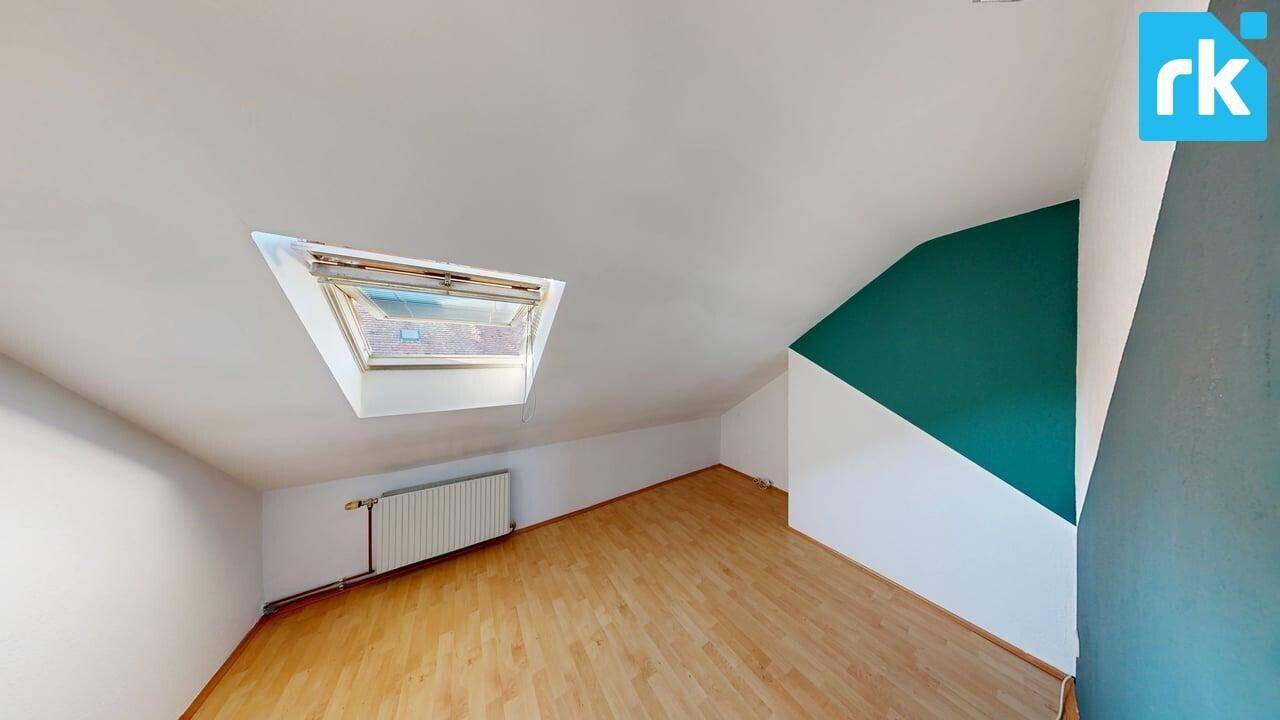 Helles Schlafzimmer im Dachgeschoss mit Holzboden, Dachschräge und einem Dachfenster.