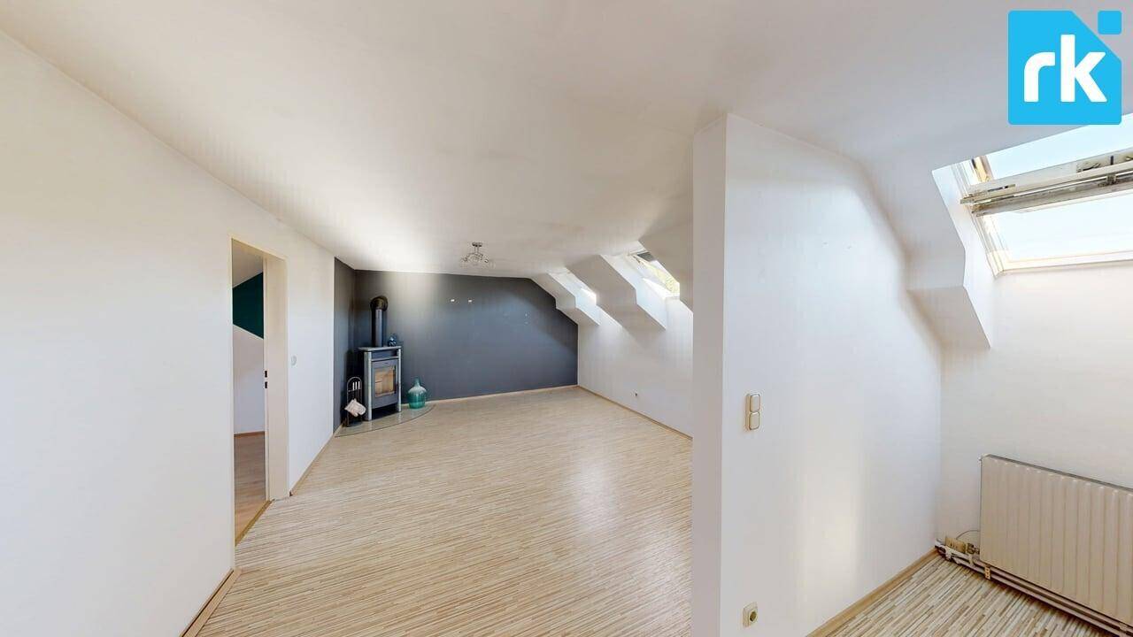 Dachgeschoss-Wohnzimmer mit Holzboden, Dachschrägen und einem modernen Holzofen.