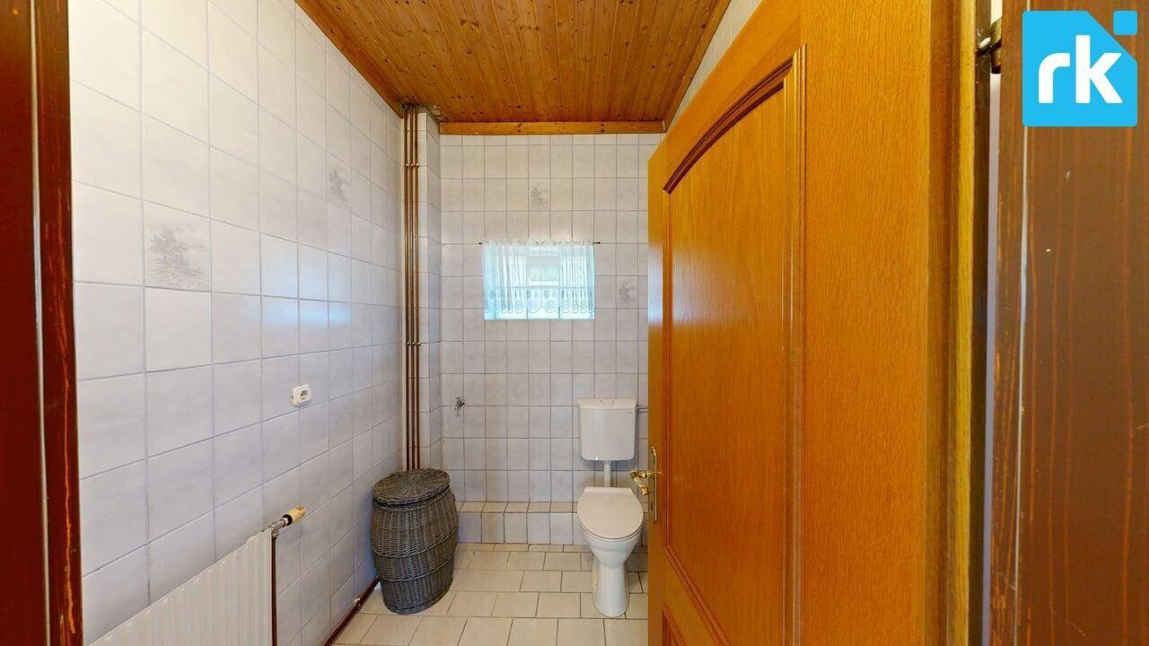 Separate Toilette mit Fliesenboden, Holzdecke und einem kleinen Fenster für Belüftung.