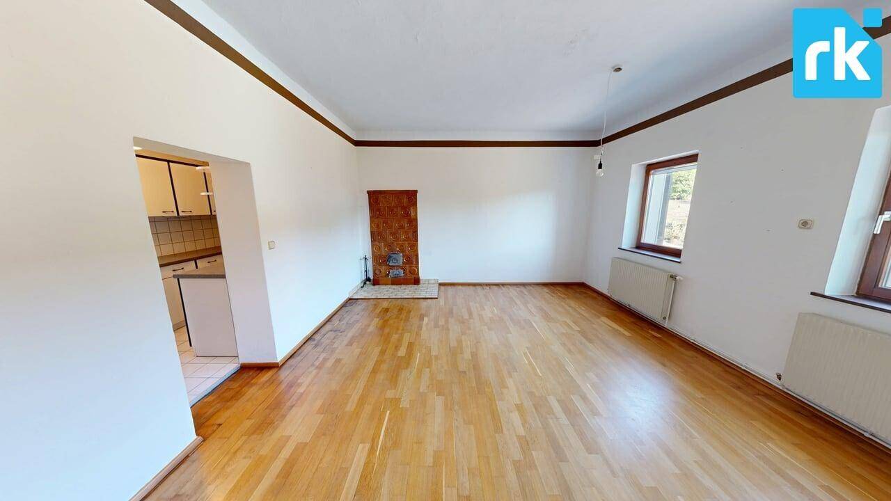 Geräumiges Wohnzimmer mit Parkettboden, zwei Fenstern und einem traditionellen Kachelofen.