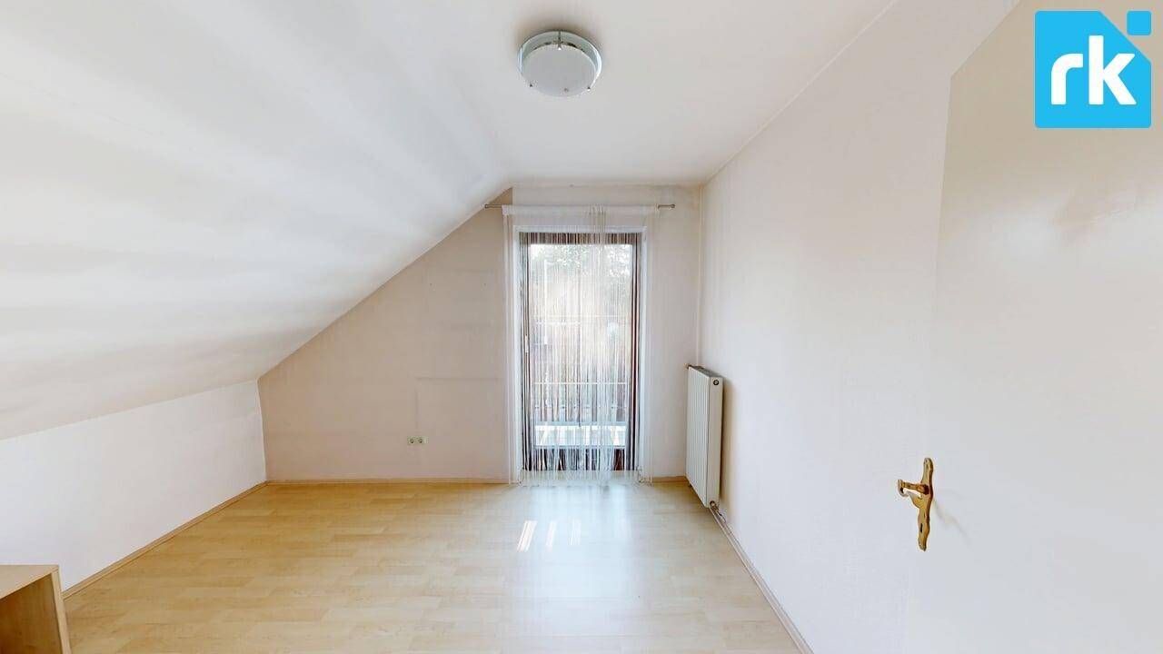 Schlafzimmer im Dachgeschoss mit Holzboden, Dachschräge und einem großen Fenster.