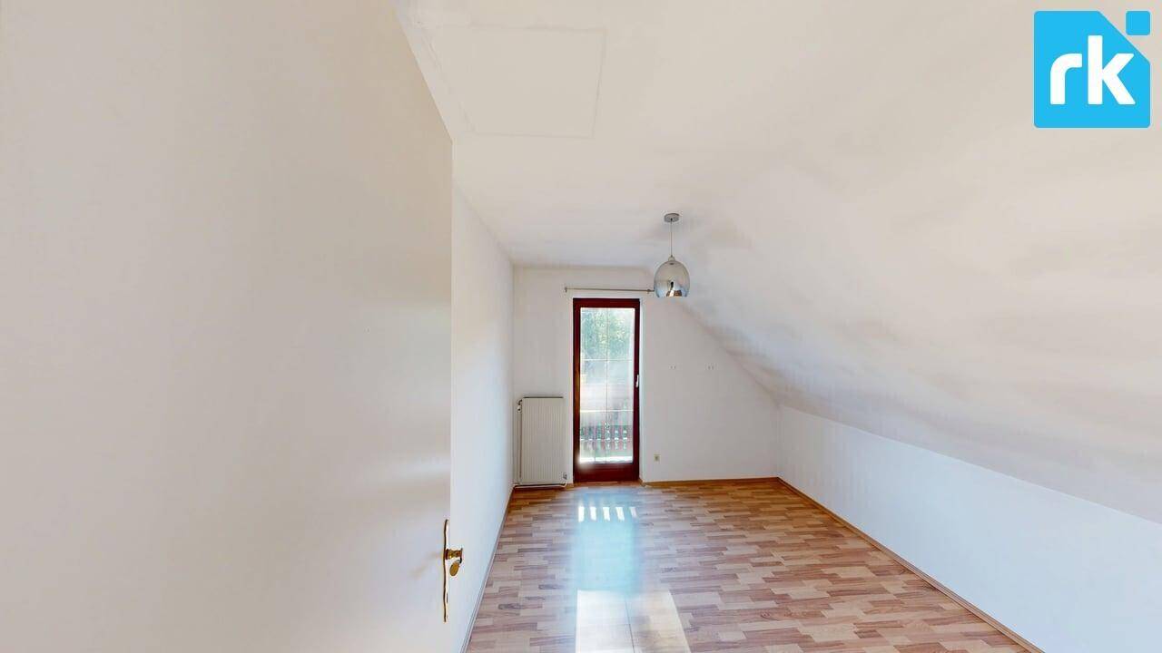 Schlafzimmer im Dachgeschoss mit Holzboden, Dachschräge und Zugang zu einem kleinen Balkon.