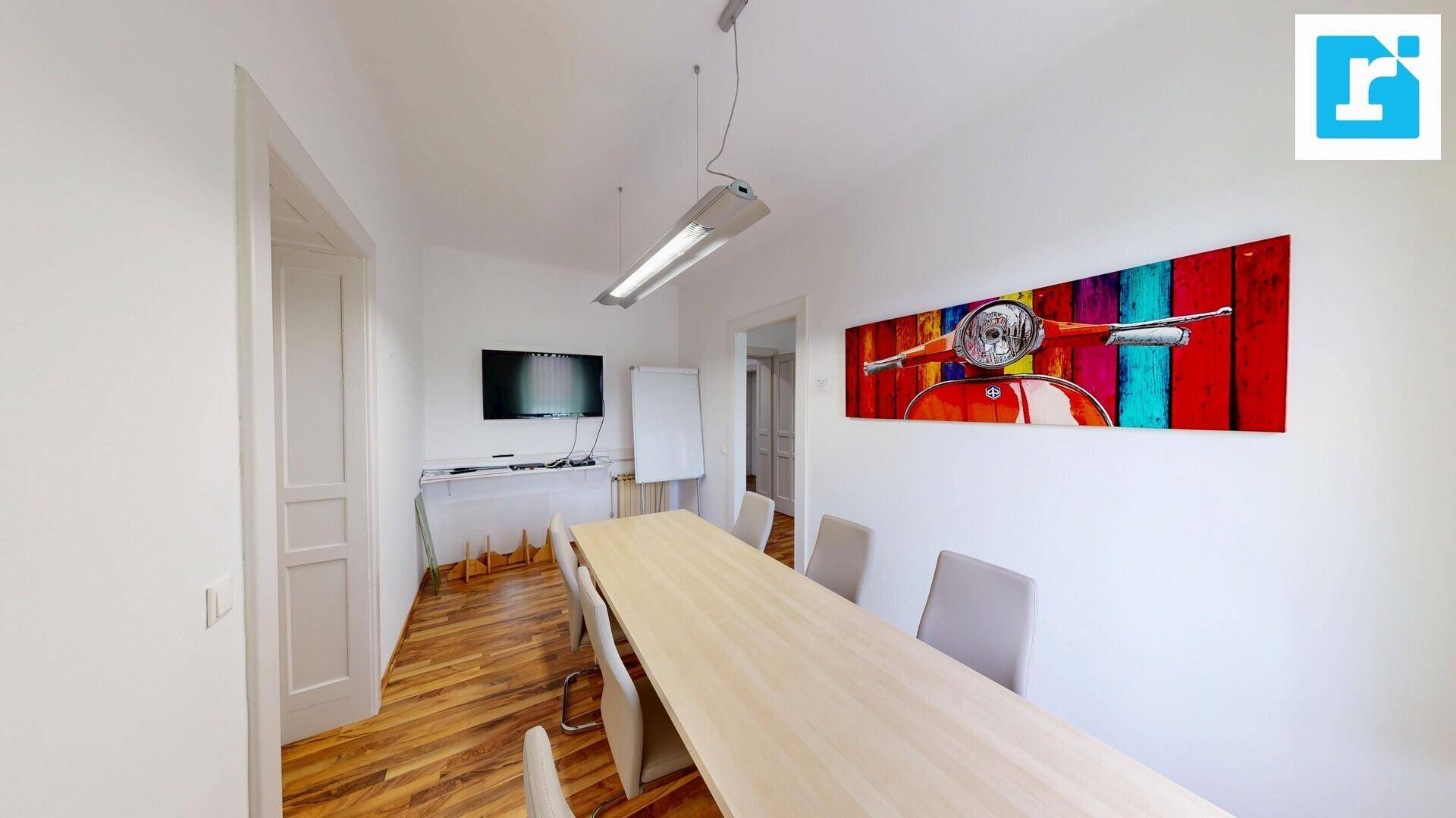 Besprechungsraum mit einem großen Tisch, einem Wandfernseher und farbenfroher Wandkunst, ideal für Präsentationen.