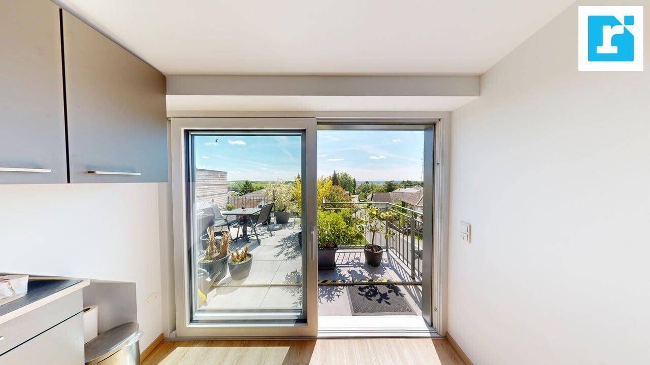 Blick aus der Dachgeschosswohnung durch große Schiebetüren auf eine möblierte Terrasse mit Weitblick.