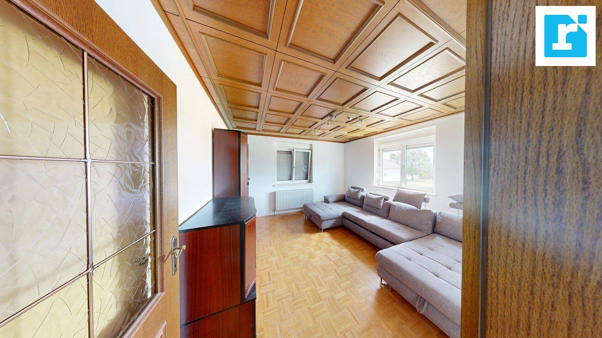 Geräumiges Wohnzimmer mit Holzkassettendecke, Parkettboden und großem Ecksofa.