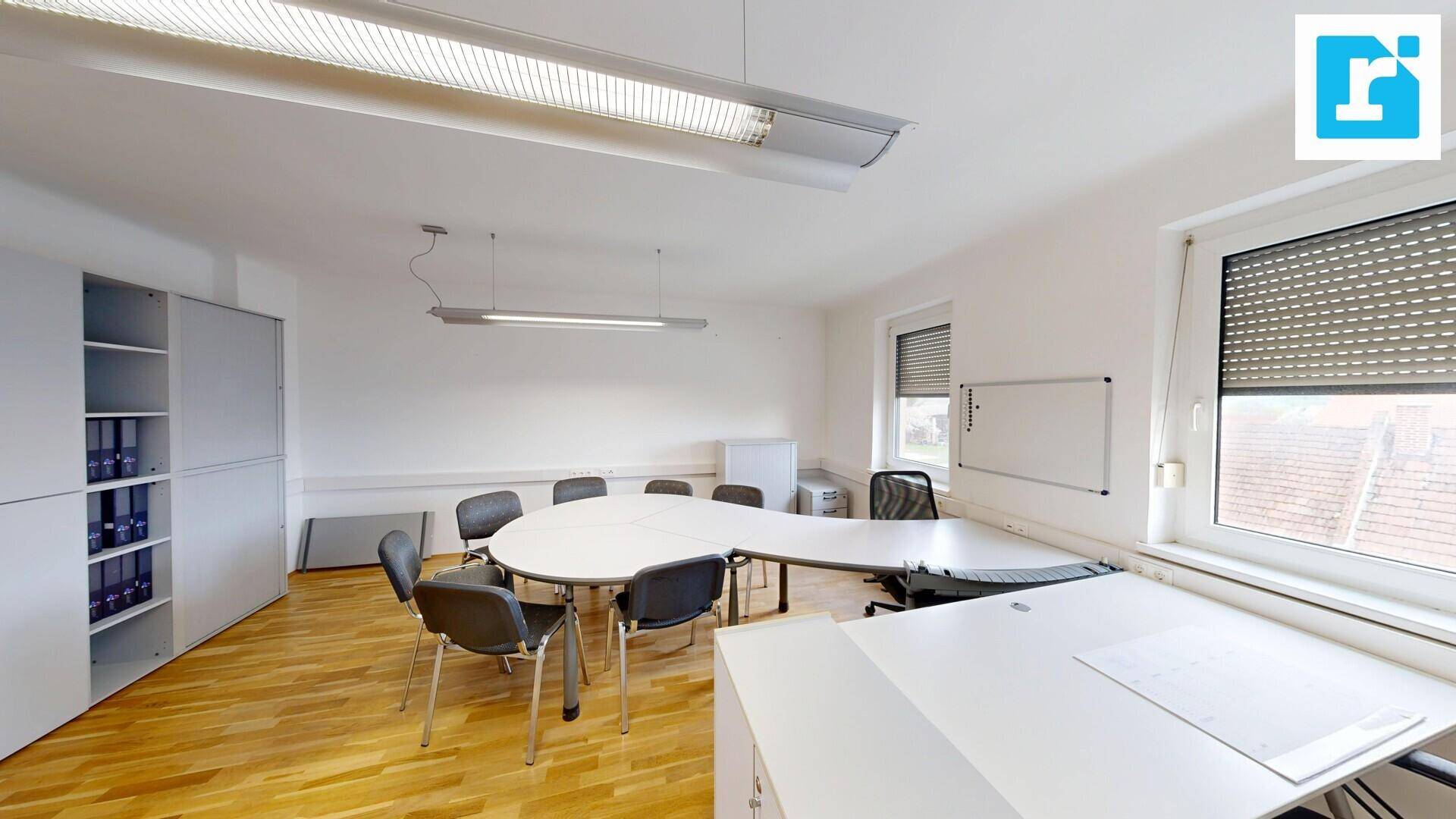 Helles Büro mit Holzboden, einem runden Besprechungstisch und Fenstern mit Rollläden für optimale Lichtregulierung.