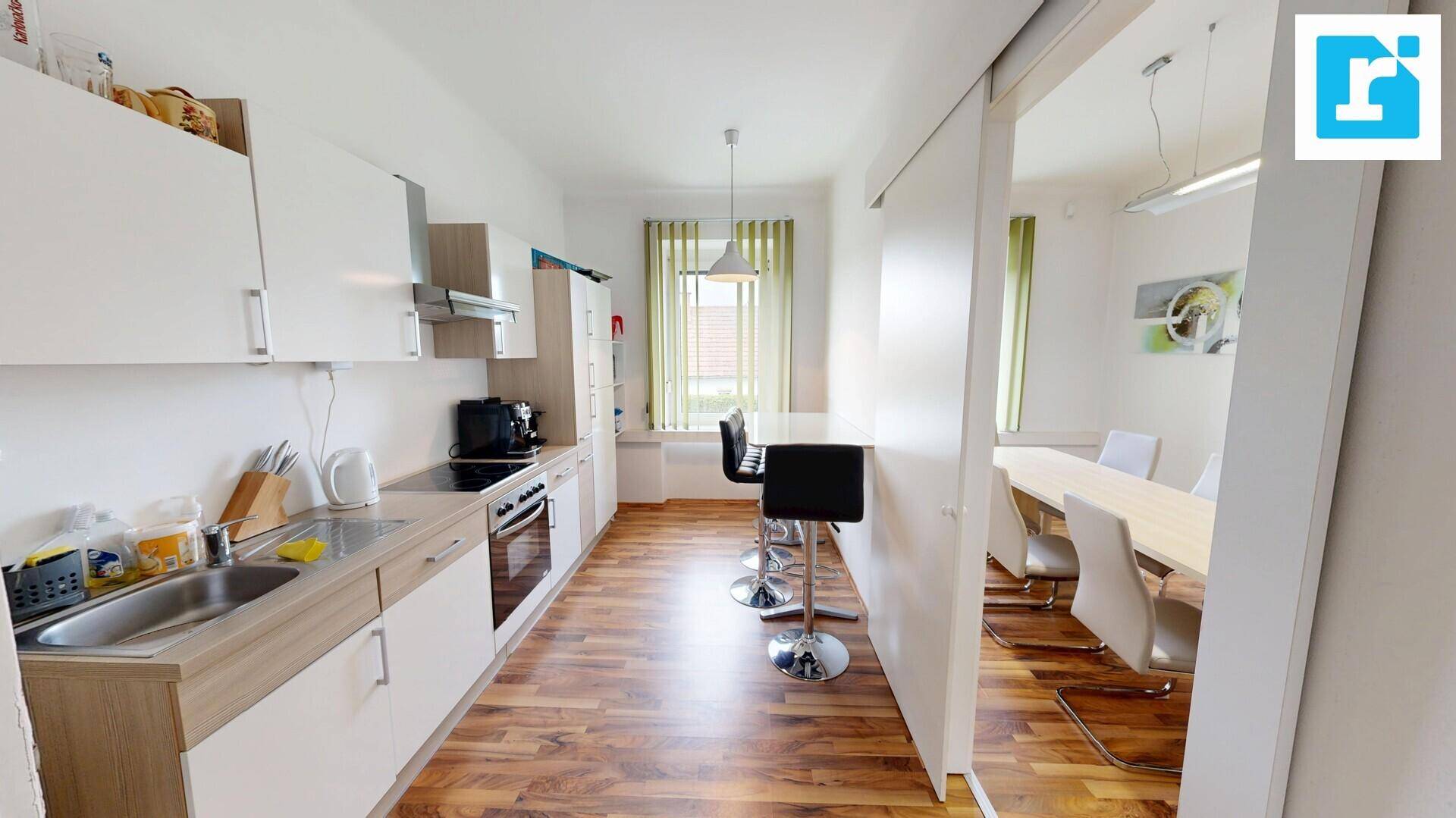 Moderne Küchenzeile mit Barhockern und angrenzendem Besprechungsraum mit Holzboden und Fenster.