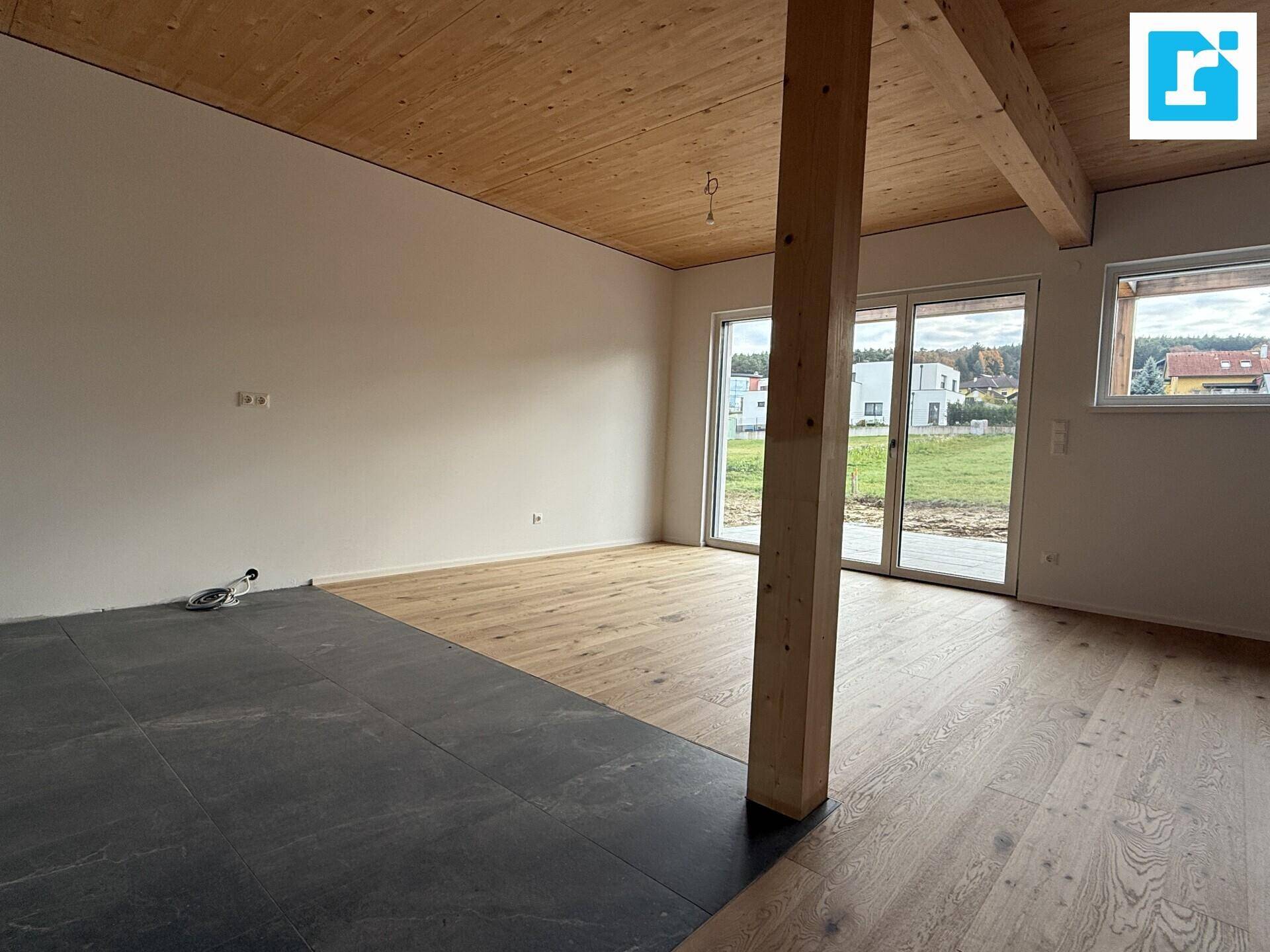 Geräumiges Wohnzimmer mit Holzbalken, Parkett und Blick ins Grüne.