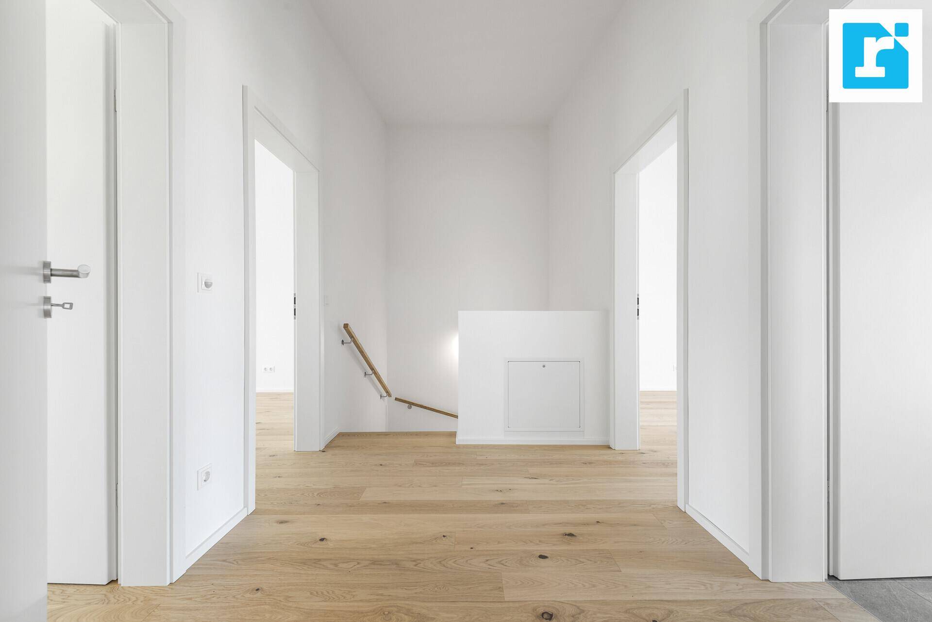 Langer, heller Flur mit Holzboden und Treppenabgang, der zu weiteren Räumen führt.