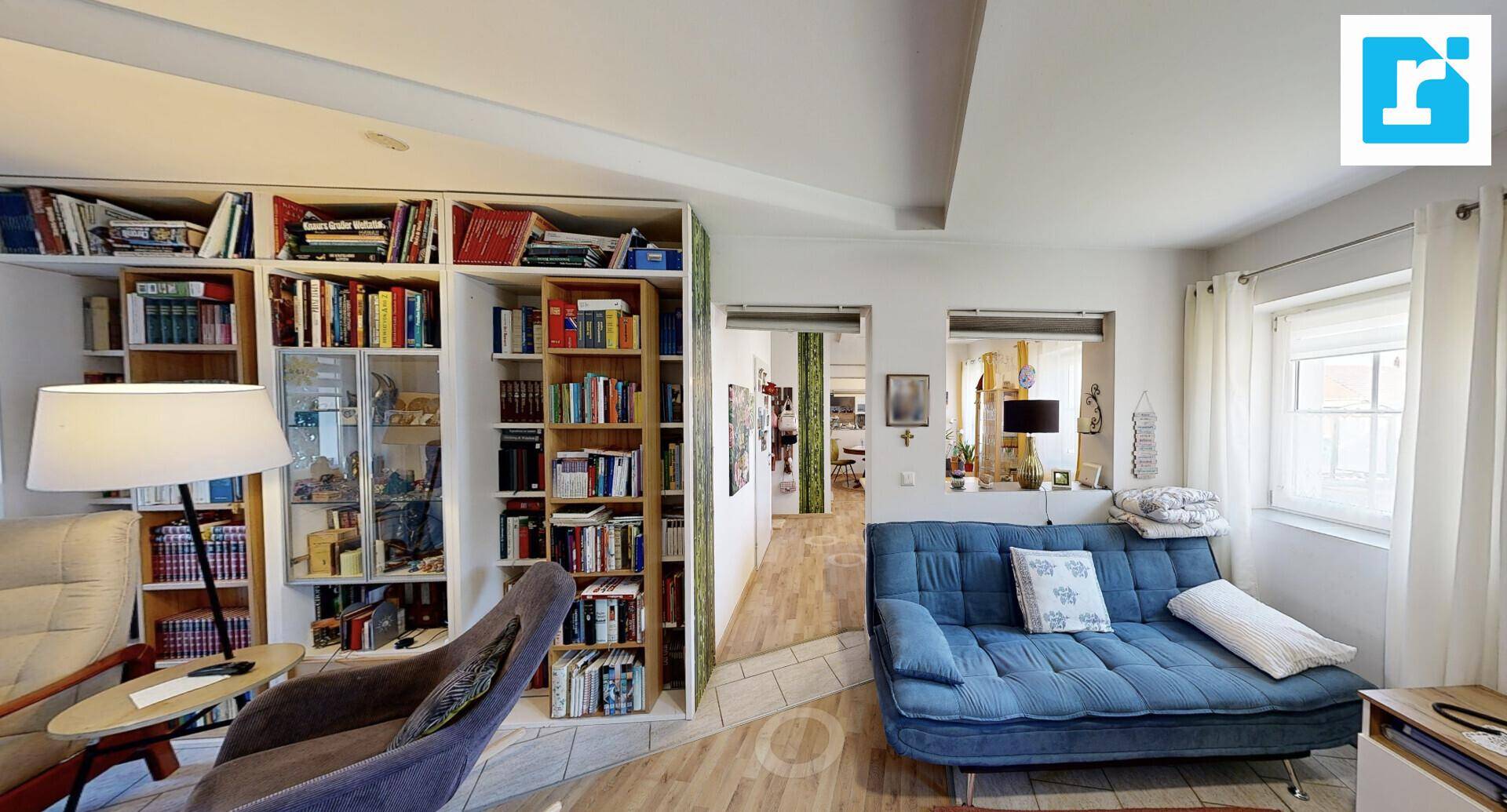 Gemütliches Wohnzimmer mit blauem Sofa, großer Bücherwand und Holzboden.