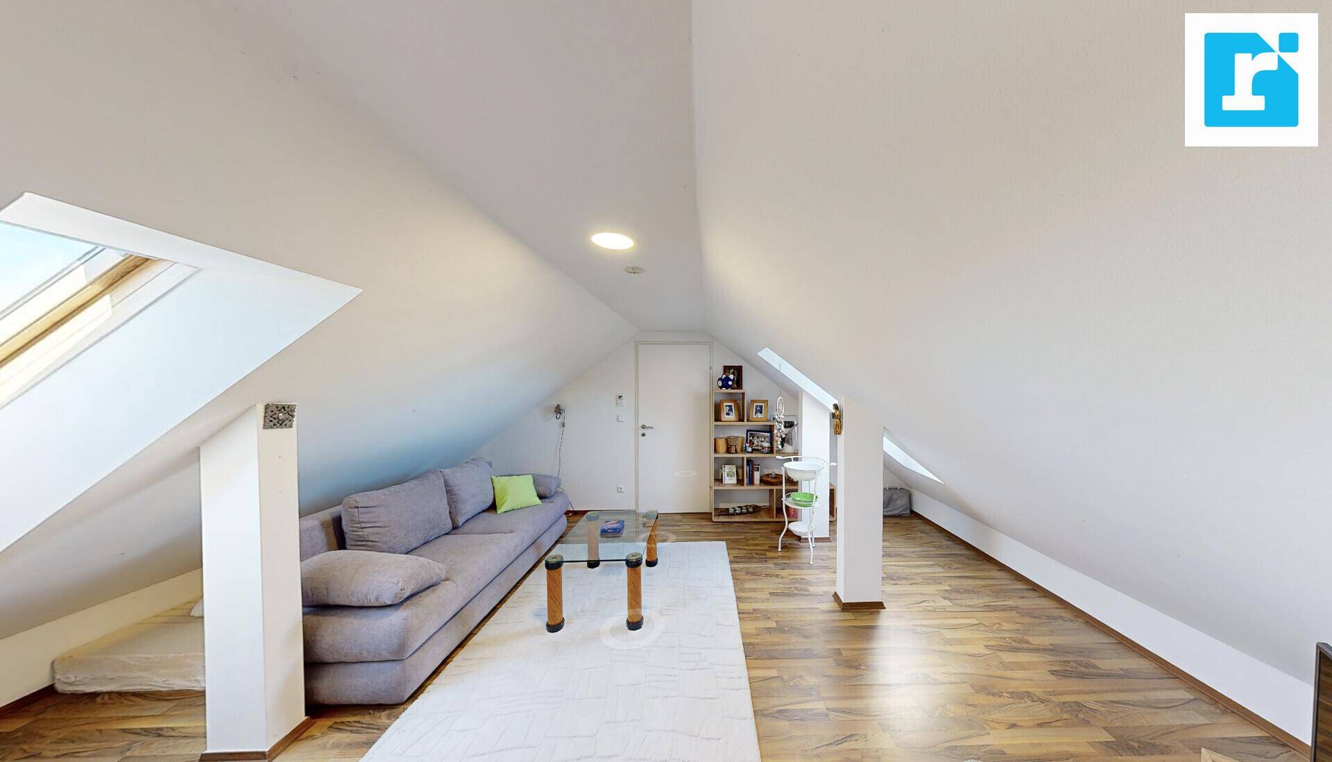 Heller Dachbodenbereich mit schrägen Decken, Sofa und einem Dachfenster.
