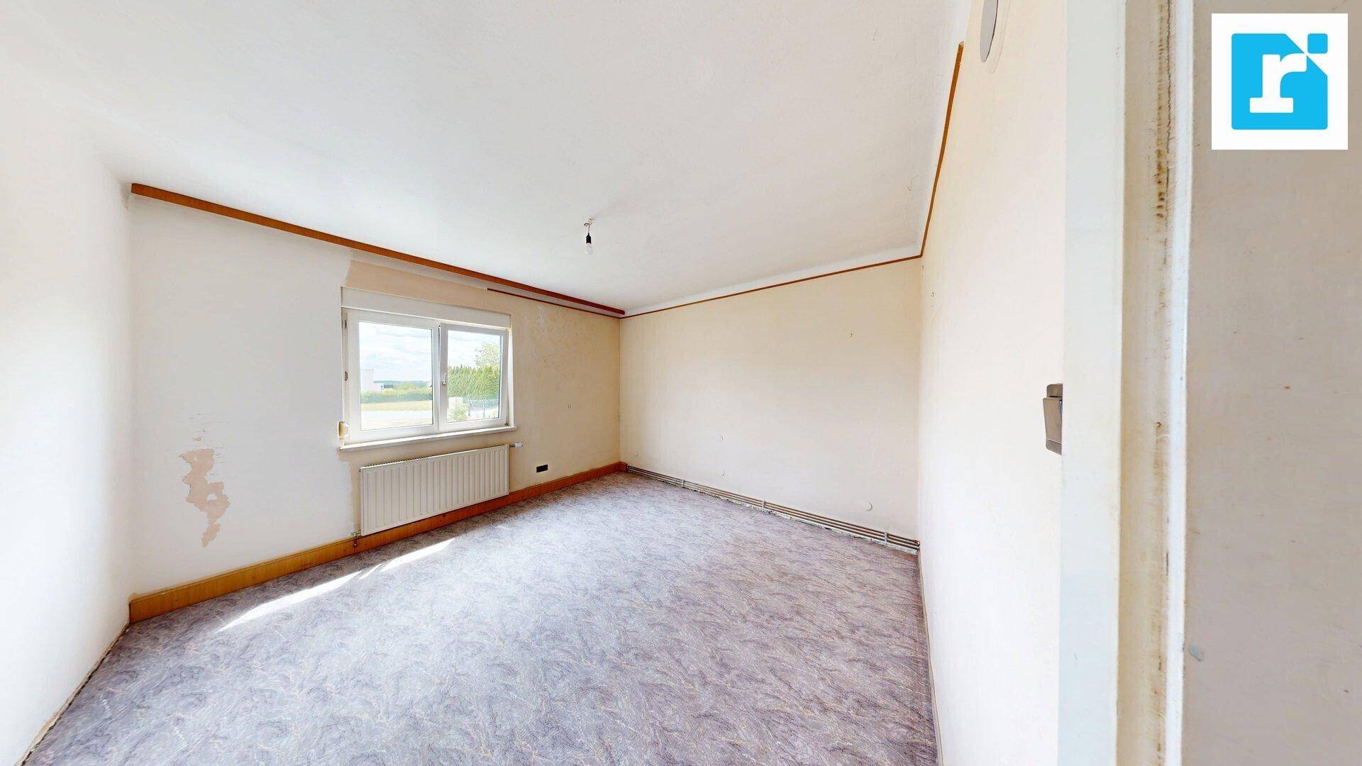Leeres Zimmer mit Teppichboden und Fenster, das viel Tageslicht hereinlässt.