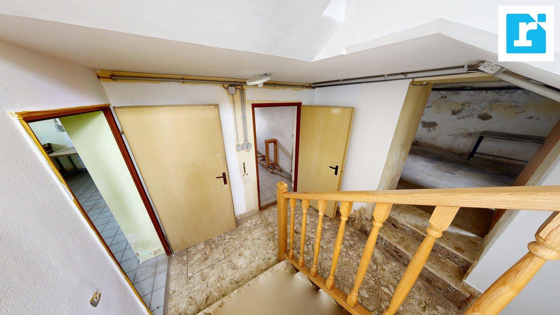 Blick auf einen Kellerflur mit mehreren Türen und einer Holztreppe, die in die oberen Stockwerke führt.