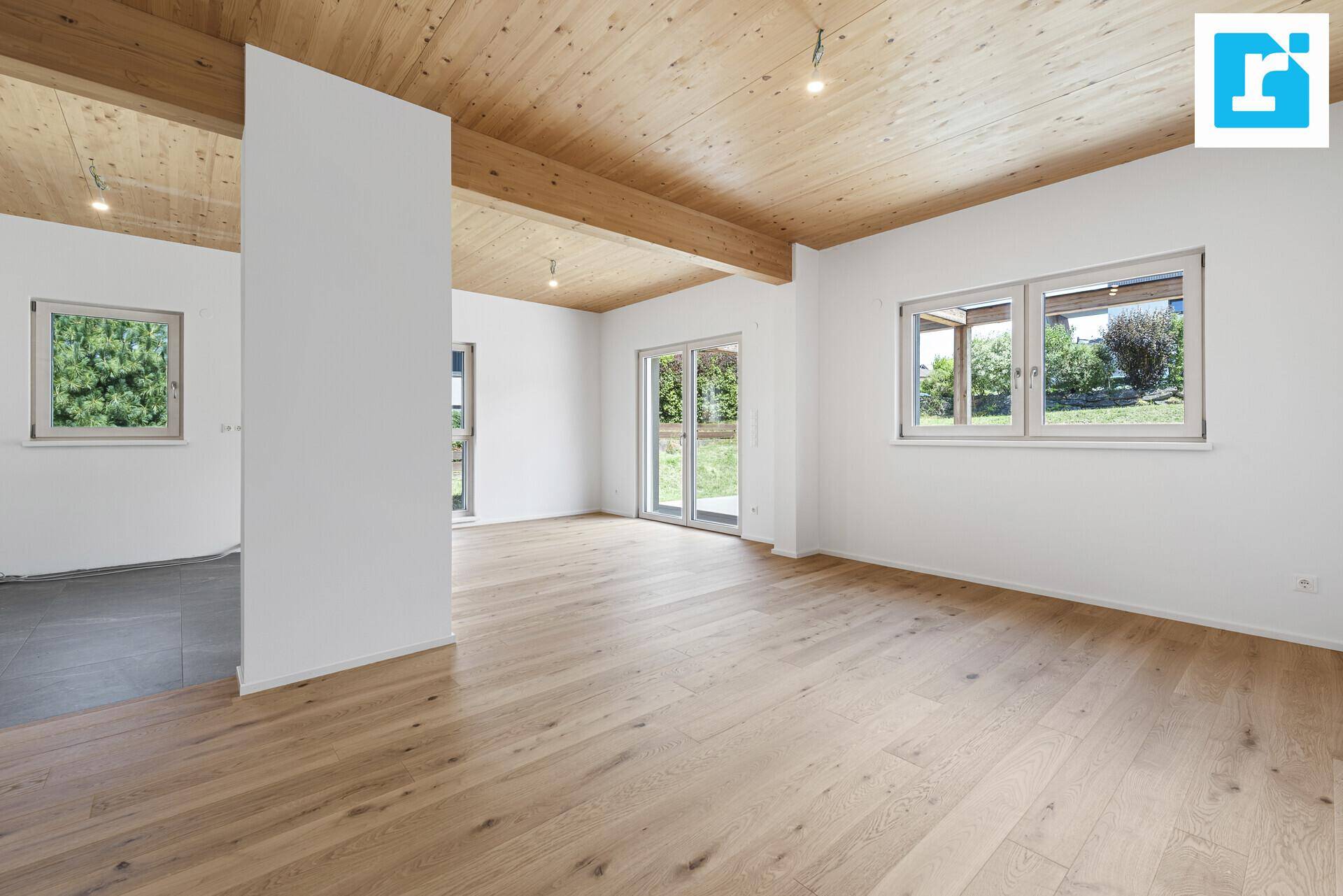 Heller, offener Wohnbereich mit Holzbalkendecke, Parkettboden und Zugang zum Garten.