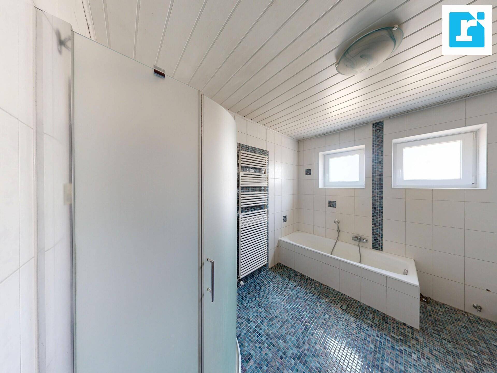 Badezimmer mit Duschkabine, Badewanne, Handtuchheizkörper und blauen Mosaikfliesen.