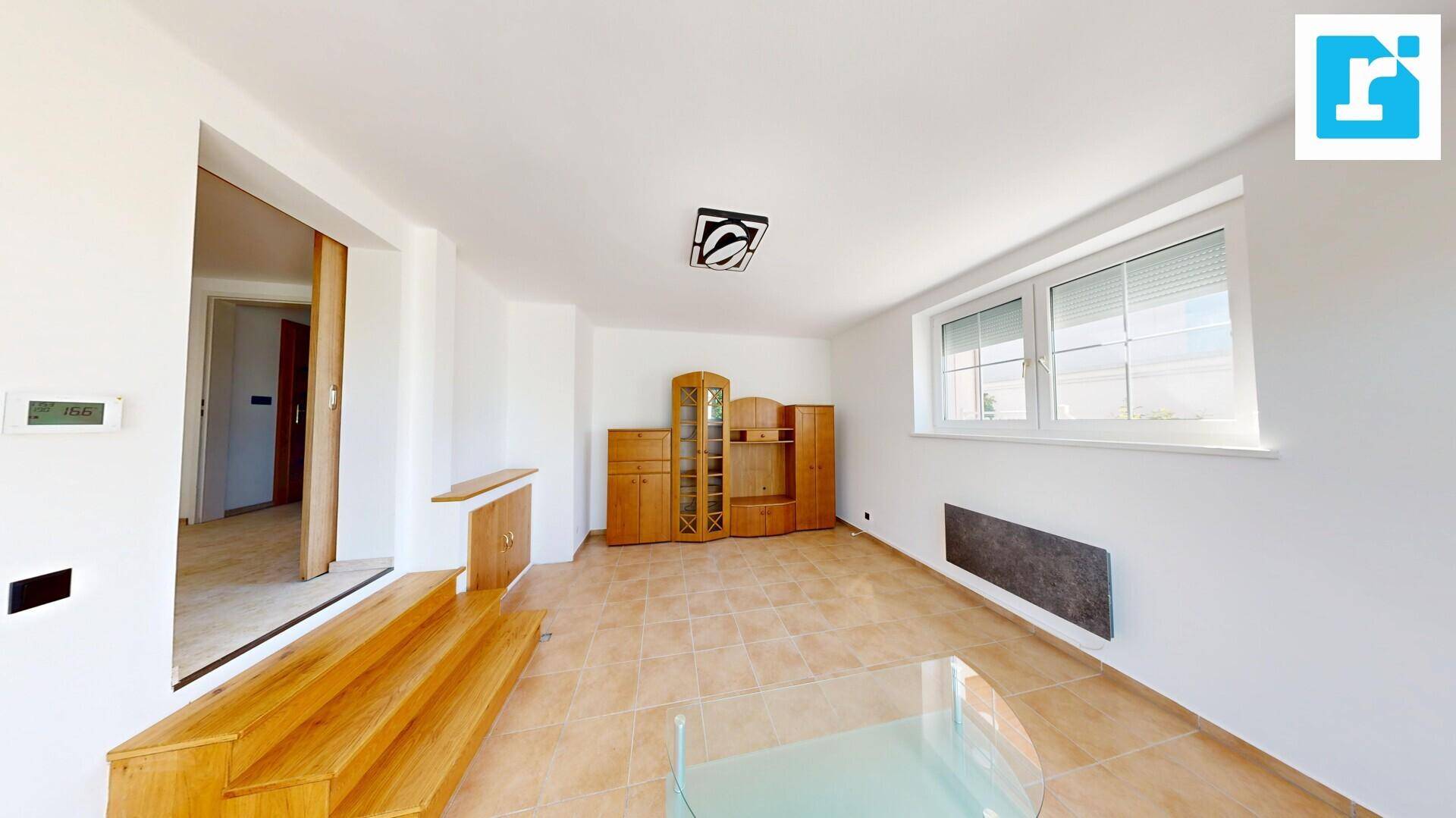 Geräumiges Wohnzimmer mit Fliesenboden, großen Fenstern und traditionellen Holzmöbeln.