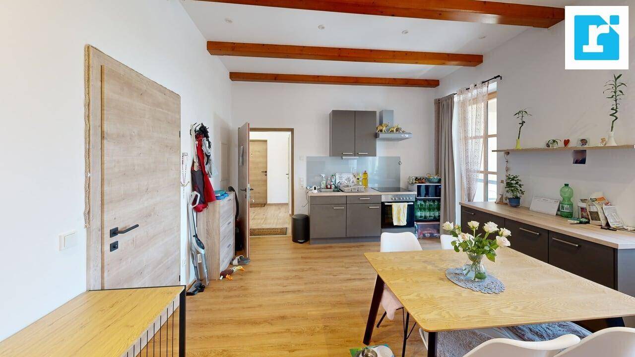 Küche mit grauen Schränken, Holzarbeitsplatten und sichtbaren Holzbalken an der Decke, Essbereich integriert.