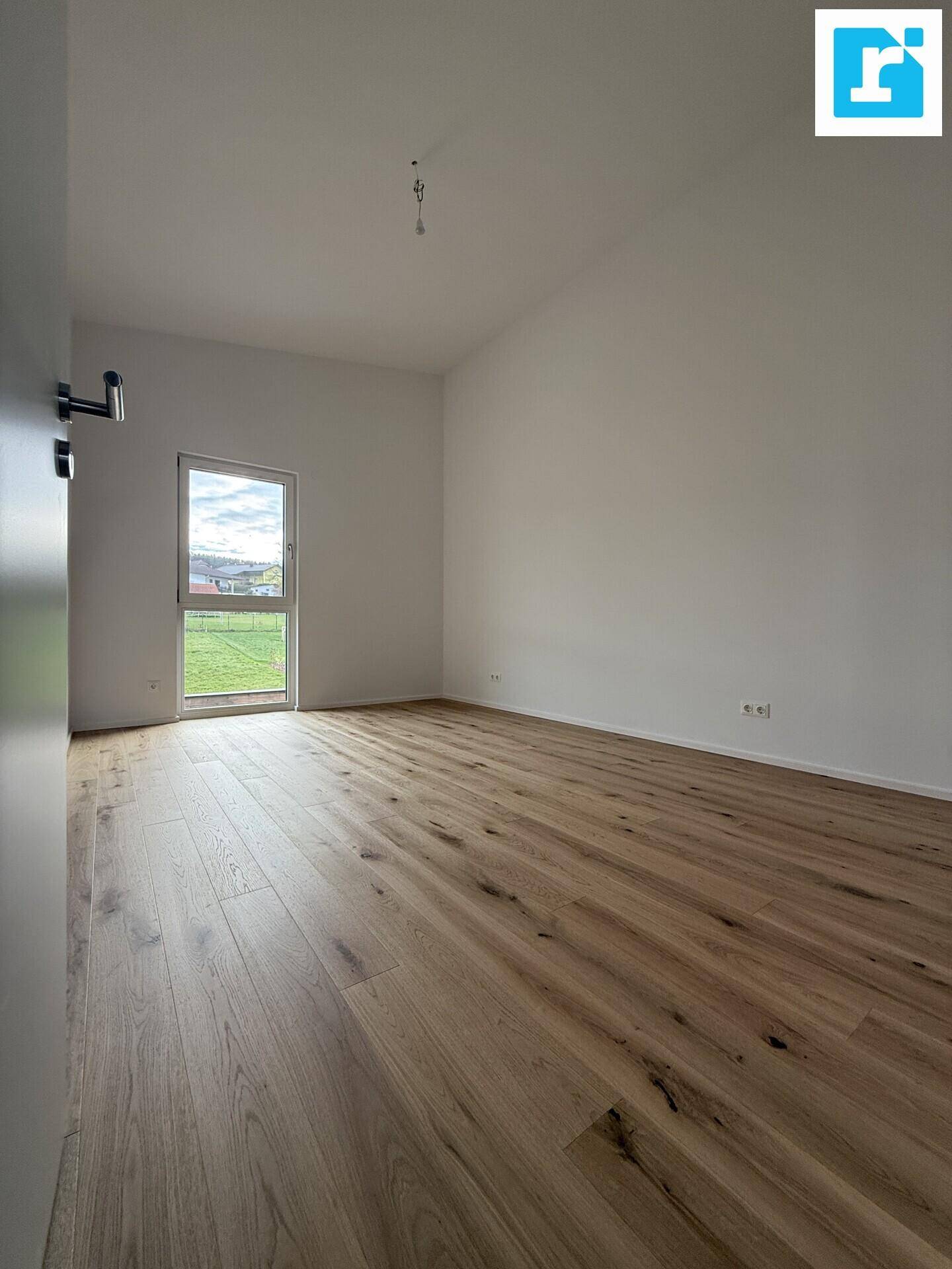 Helles Schlafzimmer mit Parkettboden und Fenster mit Blick ins Grüne.