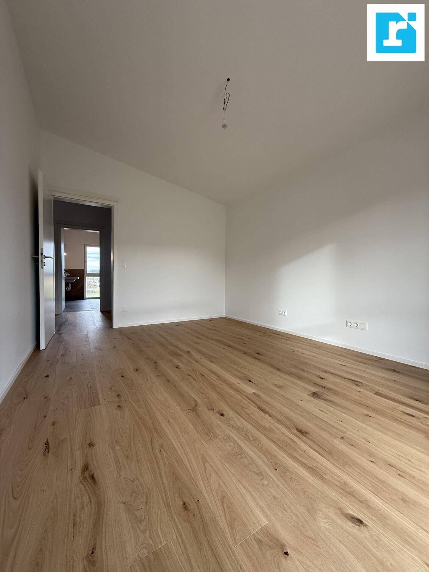 Helles Schlafzimmer mit Parkettboden und Zugang zu einem weiteren Raum.