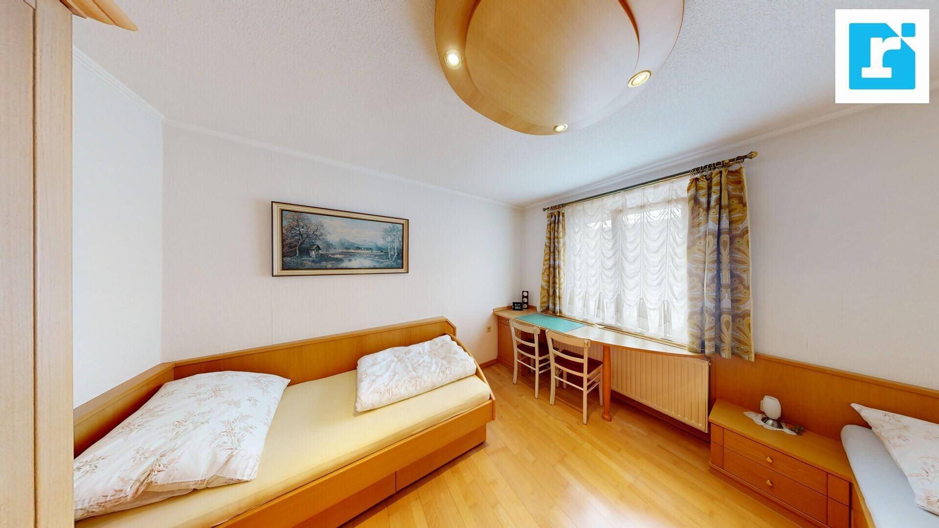 Helles Schlafzimmer mit Einzelbett, Holzboden und Schreibtisch am Fenster.