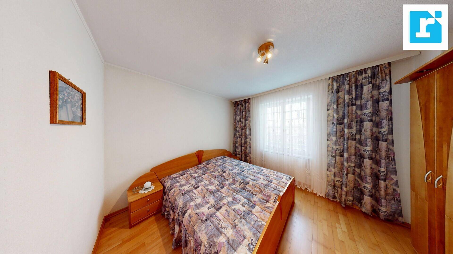 Schlafzimmer mit Doppelbett, Holzboden und Fenster mit gemusterten Vorhängen.
